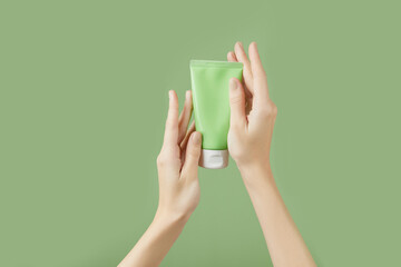 A womans hands holding a tube of lotion on a green background. Body care