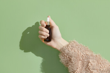 A womans hand holding a brown bottle of serum on a green background