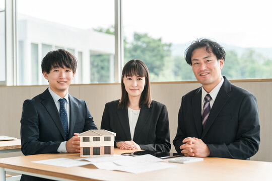 Male and female businessmen having a meeting while looking at a house model and blueprints
 - Powered by Adobe