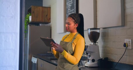 African American barista tapping tablet while checking stock at counter in olive apron smiling - Powered by Adobe