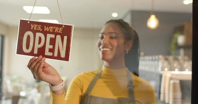 Female barista spotting CLOSED sign and flipping it to OPEN at glass shop window, copy space