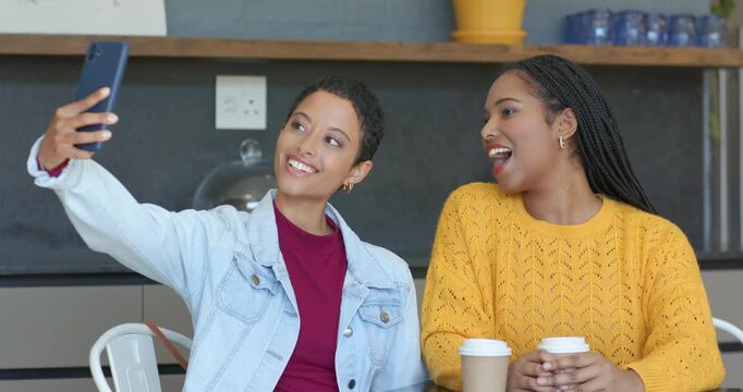 African American friends at cafe noticing phone, posing kissy selfie faces, cheering cups, laughing