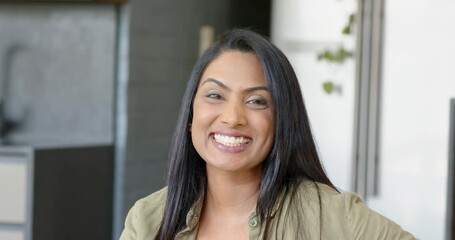 Upon seeing camera, mid adult Asian Indian woman smiling in office with cabinet and plant