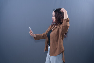 A woman in a brown shirt is taking a selfie and flexing her bicep