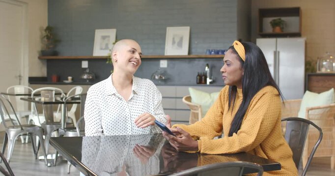 Diverse female friends hearing buzz and examining phone in kitchen, spurring swiping and gesturing