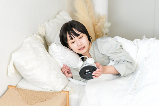 Young asian woman surprised and surprised when she sees her alarm clock (oversleep, lateness, oversleeping)
