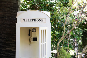A classic white telephone booth stands quietly among lush greenery, giving a charming nostalgic...