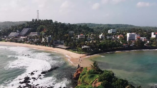 Sweeping aerial panorama revealing Mirissa Beach and Parrot Rock, showcasing pristine coastline and turquoise waters of southern Sri Lanka's tropical landscape