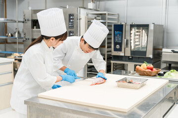 Naklejka premium Male and female staff in chef coats preparing fish (chefs, chefs, fresh market, food processing) 