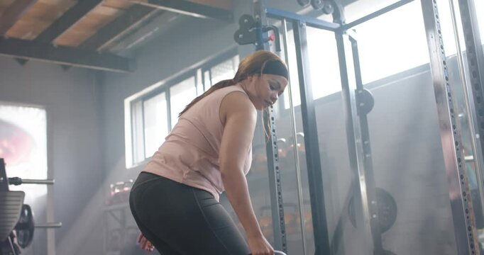 Woman bending and grasping kettlebell in gym, pulling weight toward torso and engaging back muscles
