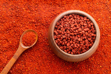 Ground or crushed organic annatto in the spoon and in the bowl - Bixa orellana