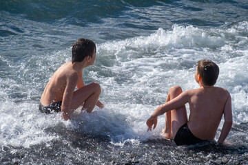 Two young children, boys splash and play in sea, ocean waves on sunny summer day, family Water activities, aquatic adventures foster curiosity and love for environment in kids