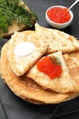 Delicious crepes with red caviar, sour cream and dill on black table, closeup