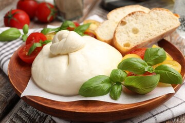 Delicious burrata cheese with basil, bread and tomatoes on wooden table, closeup