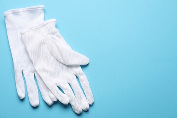 Pair of white cloth gloves on light blue background, top view. Space for text