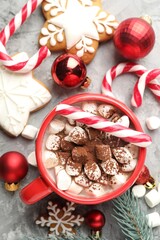 Tasty cocoa with marshmallows, candy canes, gingerbread cookies and Christmas decor on grey table, flat lay