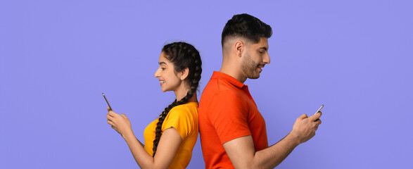 Two young adults stand back to back, smiling as they use their smartphones. They wear vibrant clothing against a bright background. The scene captures modern communication and connection.