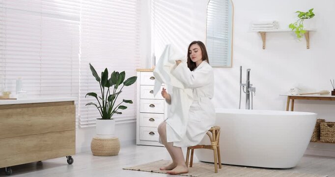 Beautiful woman in bathrobe drying hair with towel indoors