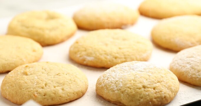 Putting powdered sugar onto tasty lemon cookies spinning on tray, closeup