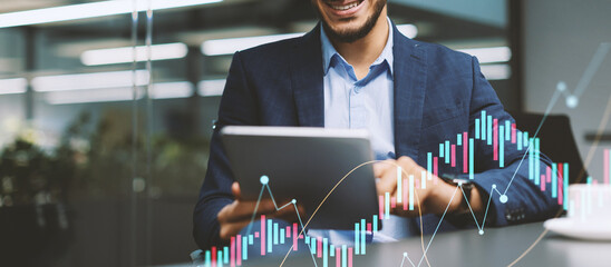 A cheerful middle eastern CEO sits at a modern office table, smiling as he uses a digital tablet to...
