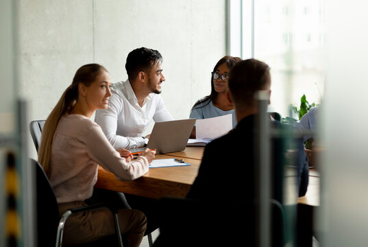 A diverse group of coworkers collaborates on a business project at a table in a modern boardroom. They share ideas and insights, engaged in teamwork during the meeting.