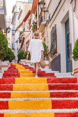Young woman in a white dress walking up the colourful Spanish Steps in the Arrabal old town district of Calpe, Spain