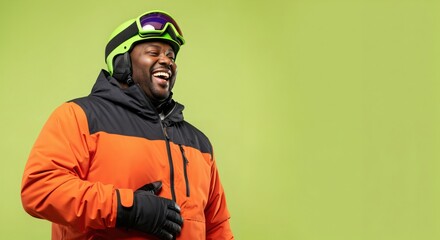 Fototapeta premium Happy African American Man Laughing in Ski Gear, Wearing Bright Orange Jacket and Green Helmet, Enjoying Winter Sports on Green Background