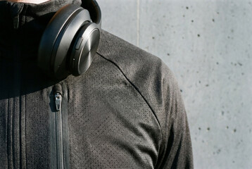 Black athletic jacket with perforated texture and wireless headphones around neck near grey wall