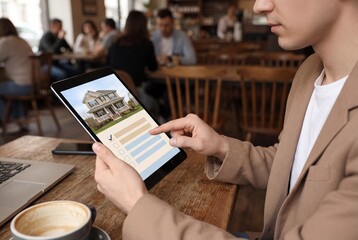 Man holding digital tablet searching for new house online while sitting at wooden table in cafe