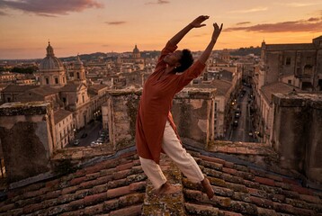Graceful black woman dancing on rooftop overlooking historic city during beautiful sunset