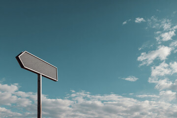Textured grey directional arrow sign on a pole, pointing left, against a teal blue sky with white clouds.