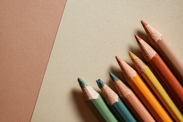 Close-up of colored pencils in warm, earthy tones, resting on contrasting brown and beige paper backgrounds. Art supplies.