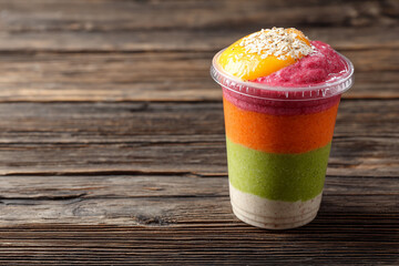 Vibrant multi-layered smoothie bowl with fruit and oats topping on a rustic wooden table. Healthy breakfast.