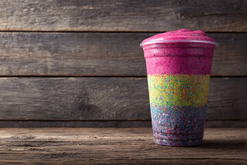 Multi-layered, brightly colored smoothie cup with sparkling layers sitting on a rustic wooden table. Healthy, vibrant, delicious beverage.
