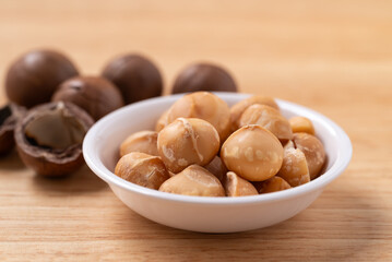 Peeled macadamia nuts in a bowl on wooden background