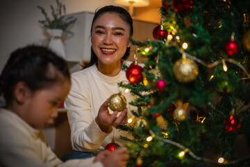 mother and toddler girl decorating Christmas tree in home at night