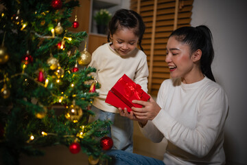 mother and toddler girl with gift box and Christmas tree in home at night