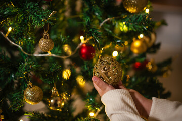 close up hand of childl decorating toy ball on Christmas tree in home at night