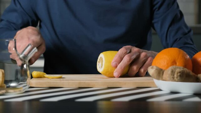 Close-up view of man cutting fresh lemon on wooden cutting board, juicy yellow fruit preparation for vitamin drink and healthy lifestyle concept