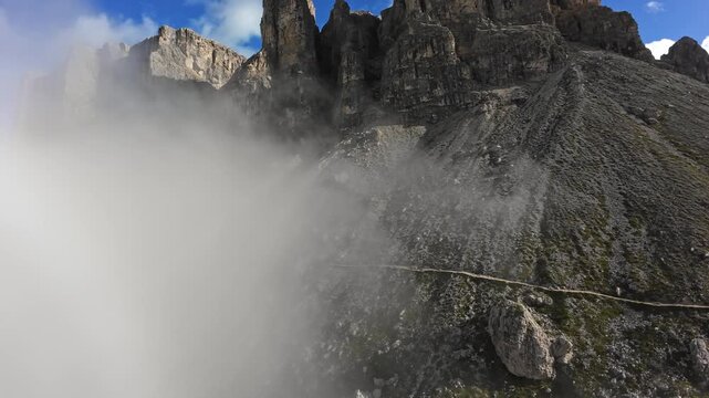 fog rolling across dolomites rocky ridge, low cloud bank sweeping over stone slopes and jagged crags; aerial drone approach, climber traverse scene, via ferrata ascent moment, geologist sampling