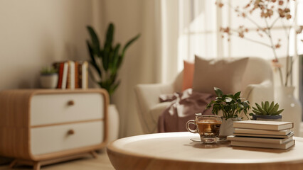 Coffee cup with books and pot plant on round wooden table across sofa and cabinet in the living room