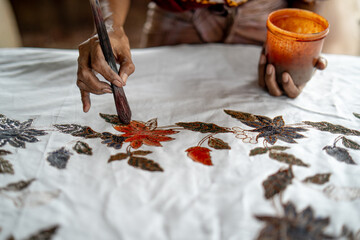 Close-up of an artisan coloring batik fabric with a brush, highlighting detailed floral designs and the precision of traditional handcraft methods. Batik CAP.
