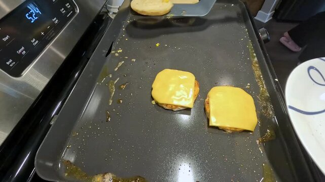 Cooking breakfast sandwiches on a griddle in a kitchen early in the morning with melted cheese and toasted buns