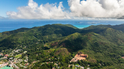 Aerial view of a verdant island with vibrant green vegetation and turquoise waters lapping at its rocky coastline. Praslin, Seychelles.