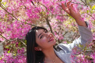 Fototapeta premium Young woman smiling among vibrant pink spring flowers
