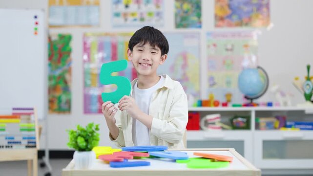 Smiling Schoolboy Holding Foam Number Five in Classroom