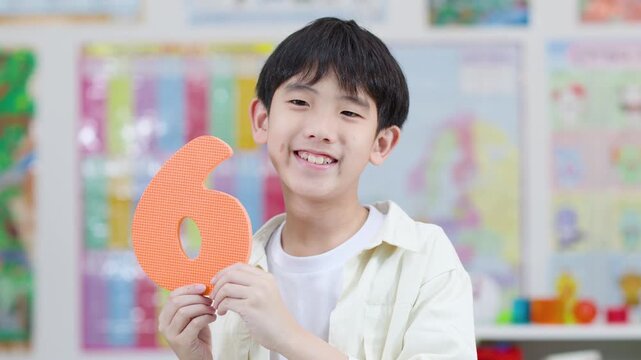 Smiling Schoolboy Holding Foam Number Six in Classroom