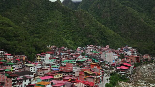 Aguas Calientes Machu Picchu town rainy season cloudy afternoon Peru aerial drone Peruvian Andes Mountains Urabumba river jungle lower highlands Inca trail citadel landscape buildings forward pan up