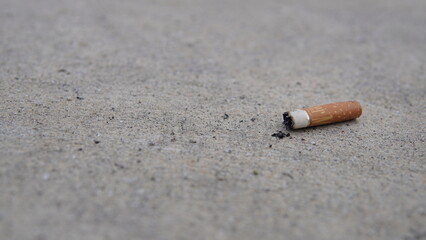 A solitary, discarded cigarette filter, marked by ash, rests abandoned on a rough concrete surface,...