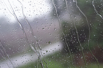 Rain drops on window glass with blurred green background. Abstract wet texture of water droplets.